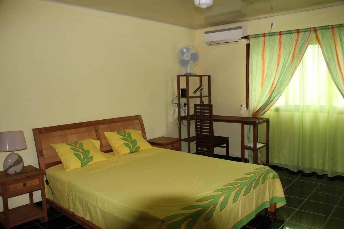 Hotelkamer met een bed, bureau, stoel, ventilator en een raam met gordijnen.