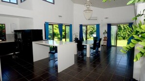 A modern kitchen with a central island, black appliances, and blue curtains. - Lausikula Chambres d'hôtes (Wallis Island)