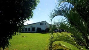 A building with a white exterior, surrounded by a well-maintained lawn and palm trees. - Lausikula Chambres d'hôtes (Wallis Island)