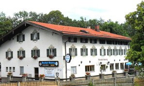 Ein weißes Gebäude mit rotem Dach, zahlreichen Fenstern mit Fensterläden und einem Schild, das es als Pension kennzeichnet.