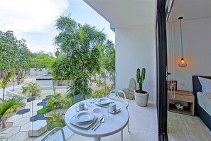 A balcony with a dining table set for two, a potted cactus, and a bed with a nightstand. - Unwind In An Exquisitely Furnished Studio , PANORAMIC C 202- By Salt - Kisses (Tulum)