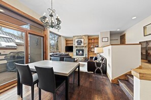 A spacious living area with a fireplace, a dining table with chairs, and a staircase leading to an upper level.