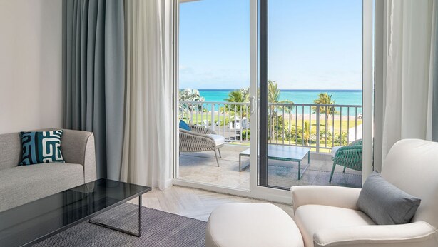 A modern living room with a glass door leading to a balcony overlooking a beach. - Ocean Terraces Penthouse 3BR (Nassau)