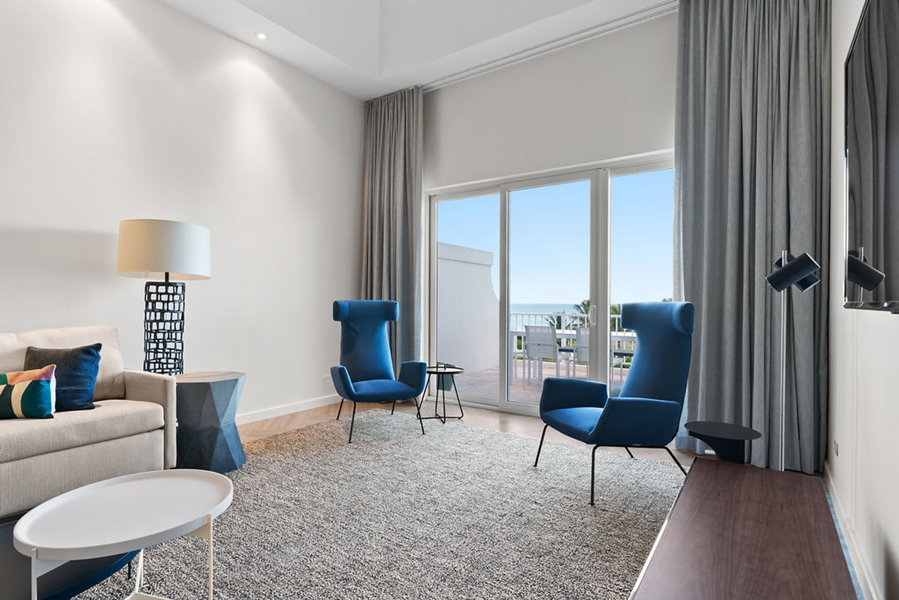 Une chambre d’hôtel moderne, dotée d’un canapé, de deux fauteuils, d’une petite table et offrant une vue sur l’extérieur.