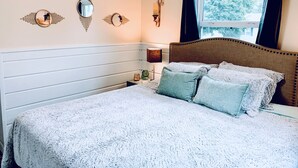 A bedroom with a bed, a nightstand, a wall-mounted lamp, and a window with curtains. - The Split Rock ~ CLEAN, Safe, Convenient Location (Bismarck)