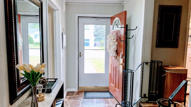 A hallway with a stone floor, a door with a window, a coat rack, and a mirror on the left. - The Split Rock ~ CLEAN, Safe, Convenient Location (Bismarck)