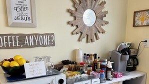 A kitchenette with a microwave, coffee maker, and various food items. There are signs on the wall, a decorative mirror, and a small shelf with a book. - The Split Rock ~ CLEAN, Safe, Convenient Location (Bismarck)