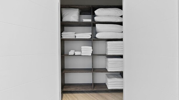 Un armario espacioso con varias repisas y cajones, que contiene toallas y ropa de cama blancos doblados ordenadamente.