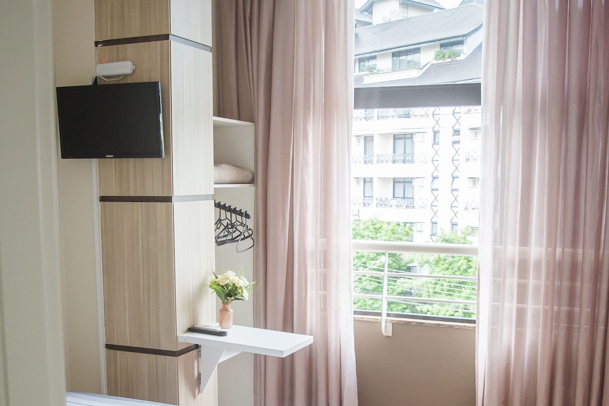 A bedroom with a bed, a wardrobe, a small table with a plant, and a window with curtains.
