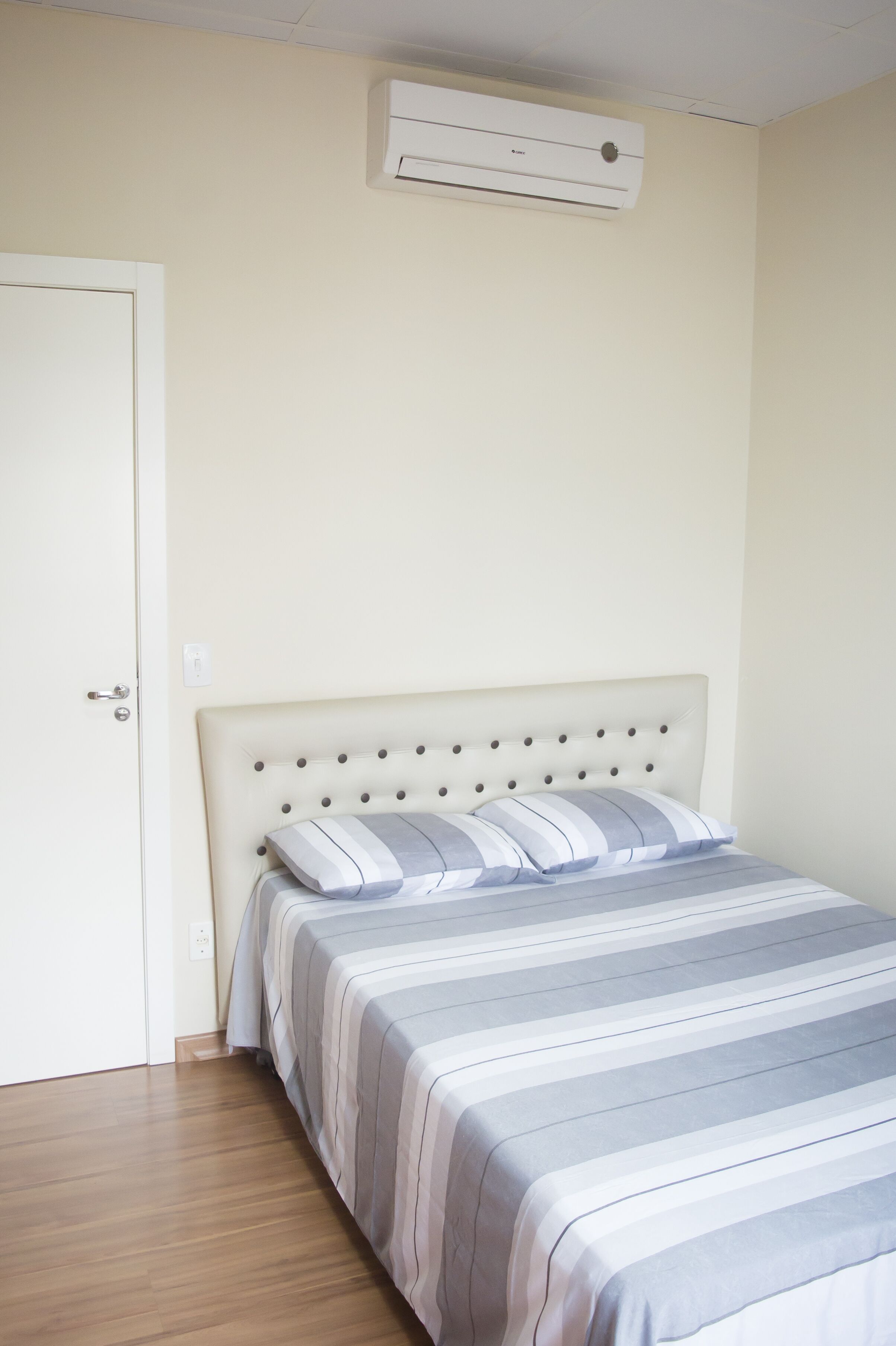 A bedroom with a bed, a door, and an air conditioning unit on the wall.