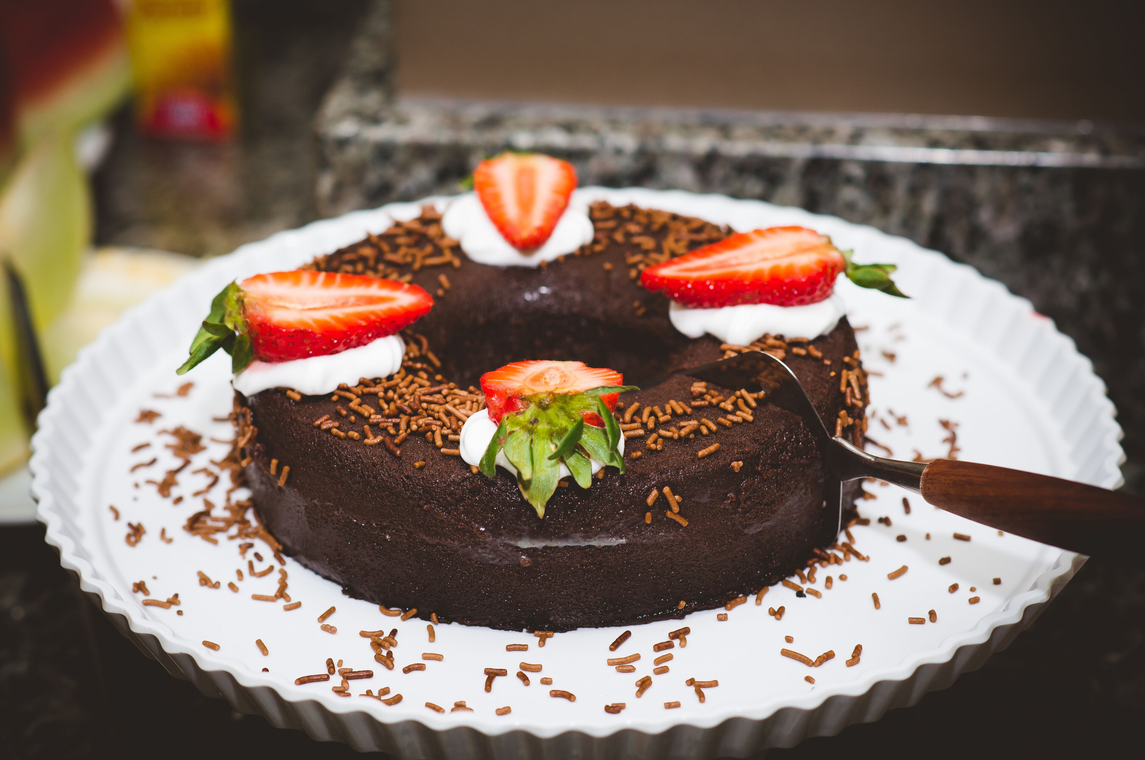 Un pastel de chocolate con fresas y grageas sobre un plato blanco.