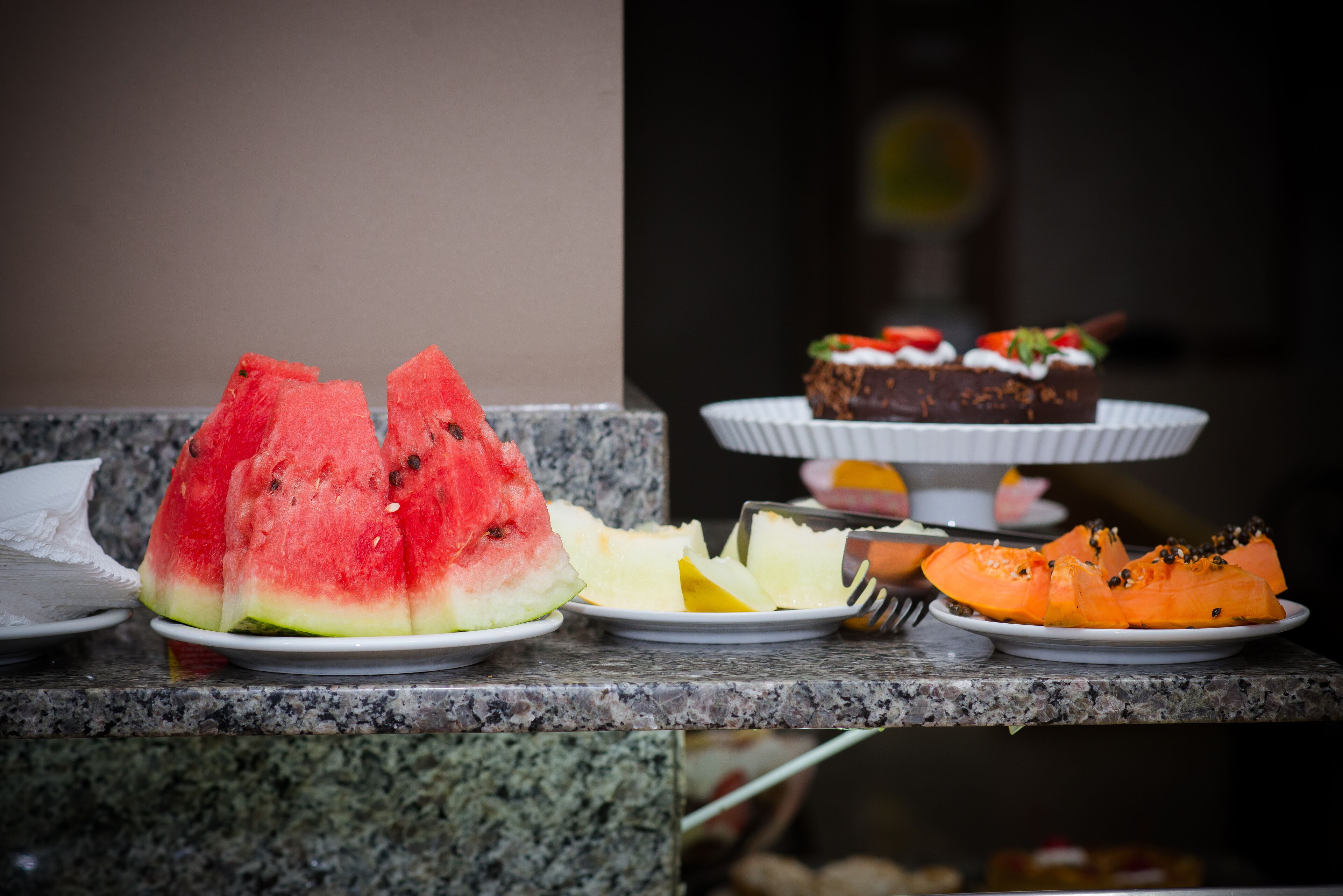 A granite countertop with plates of watermelon, pineapple, and a chocolate dessert.