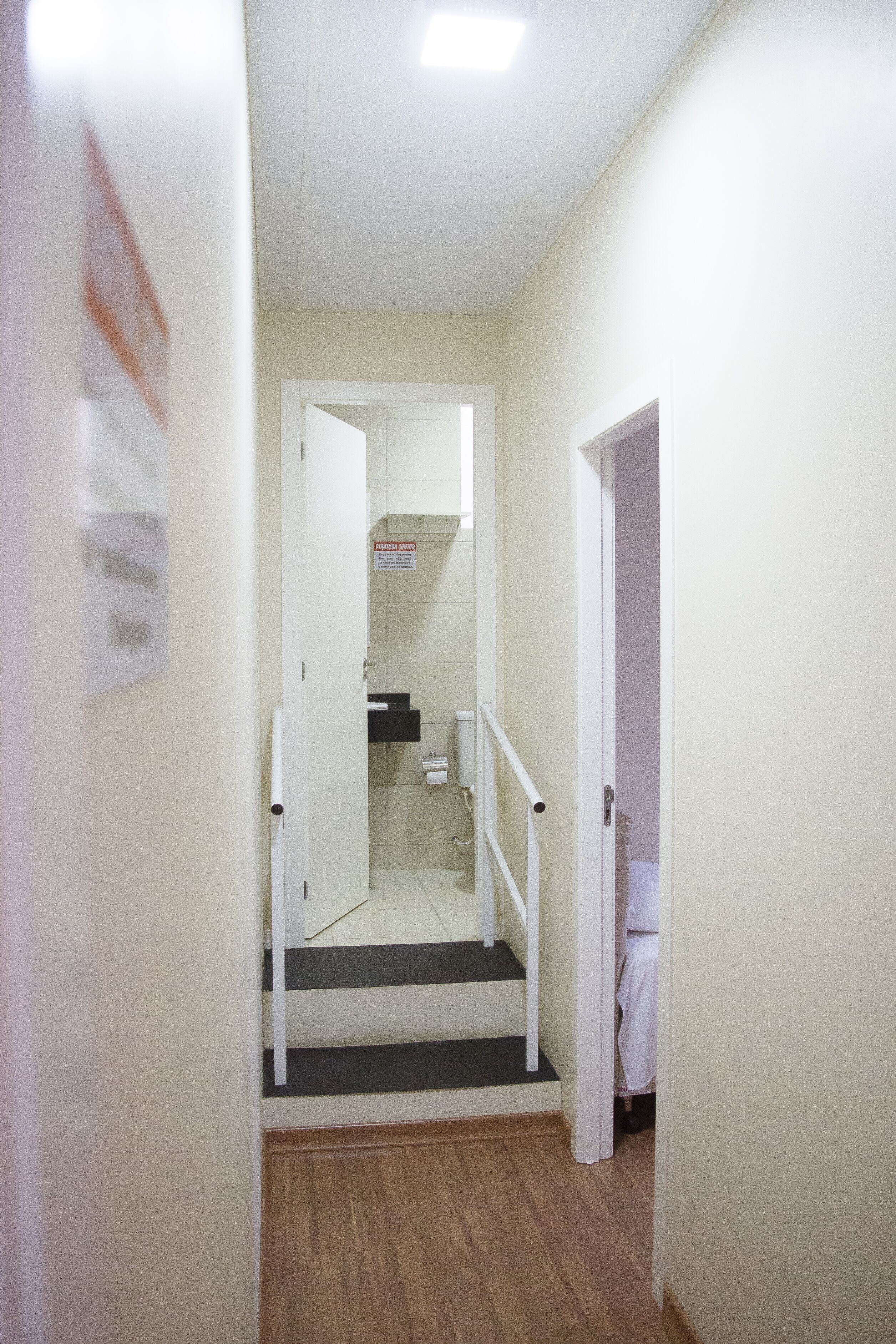 A narrow hallway with a wooden floor, a white door on the right, and a staircase leading to an upper level.