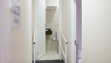 A narrow hallway with a wooden floor, a white door on the right, and a staircase leading to an upper level.
