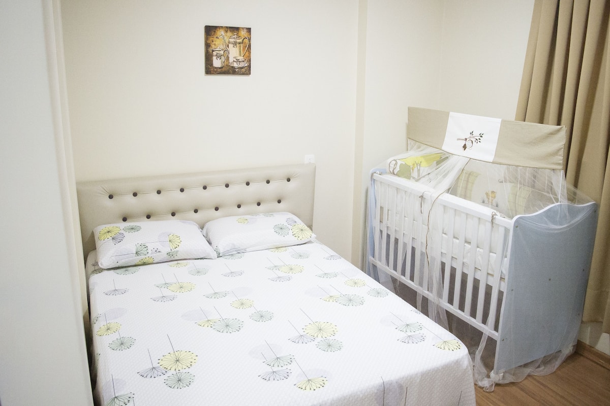 A bedroom with a bed, a crib, and a wall-mounted picture.