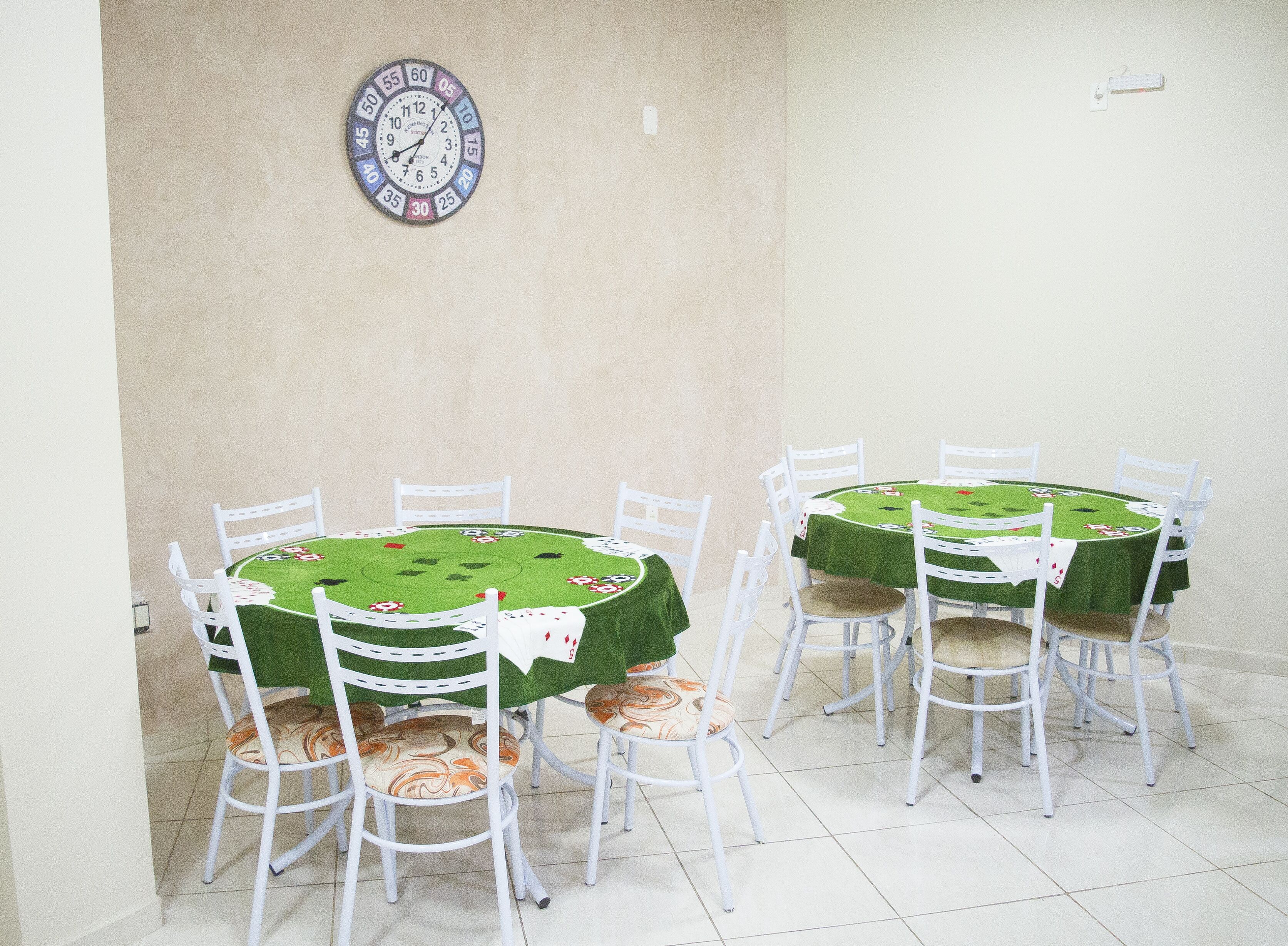Un comedor con mesas redondas cubiertas con manteles verdes, sillas blancas y un reloj de pared.
