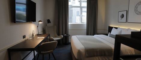 A hotel room with a bed, desk, chair, TV, and a ceiling fan.