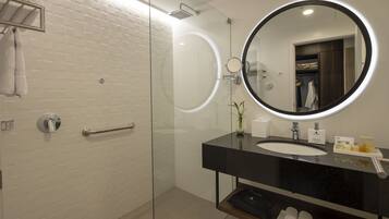 Un baño moderno con ducha de vidrio, un espejo redondo con marco negro y una encimera negra con lavabo y artículos de aseo.