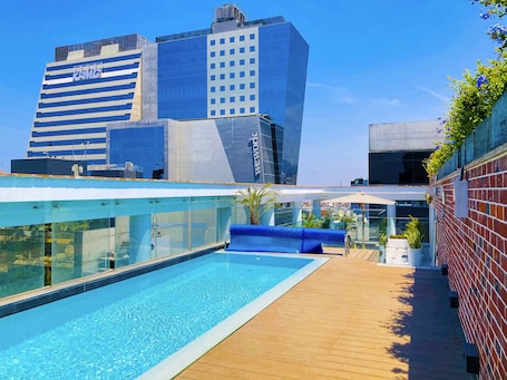 A rooftop pool with a glass barrier, a blue lounge area, and a view of surrounding high-rise buildings.. Casa Andina Premium San Isidro