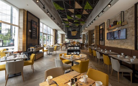 A modern cafe with yellow and grey seating, a central bar area, and large windows providing natural light.