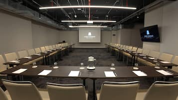 A conference room with a long table, chairs, a projector screen, and a television.
