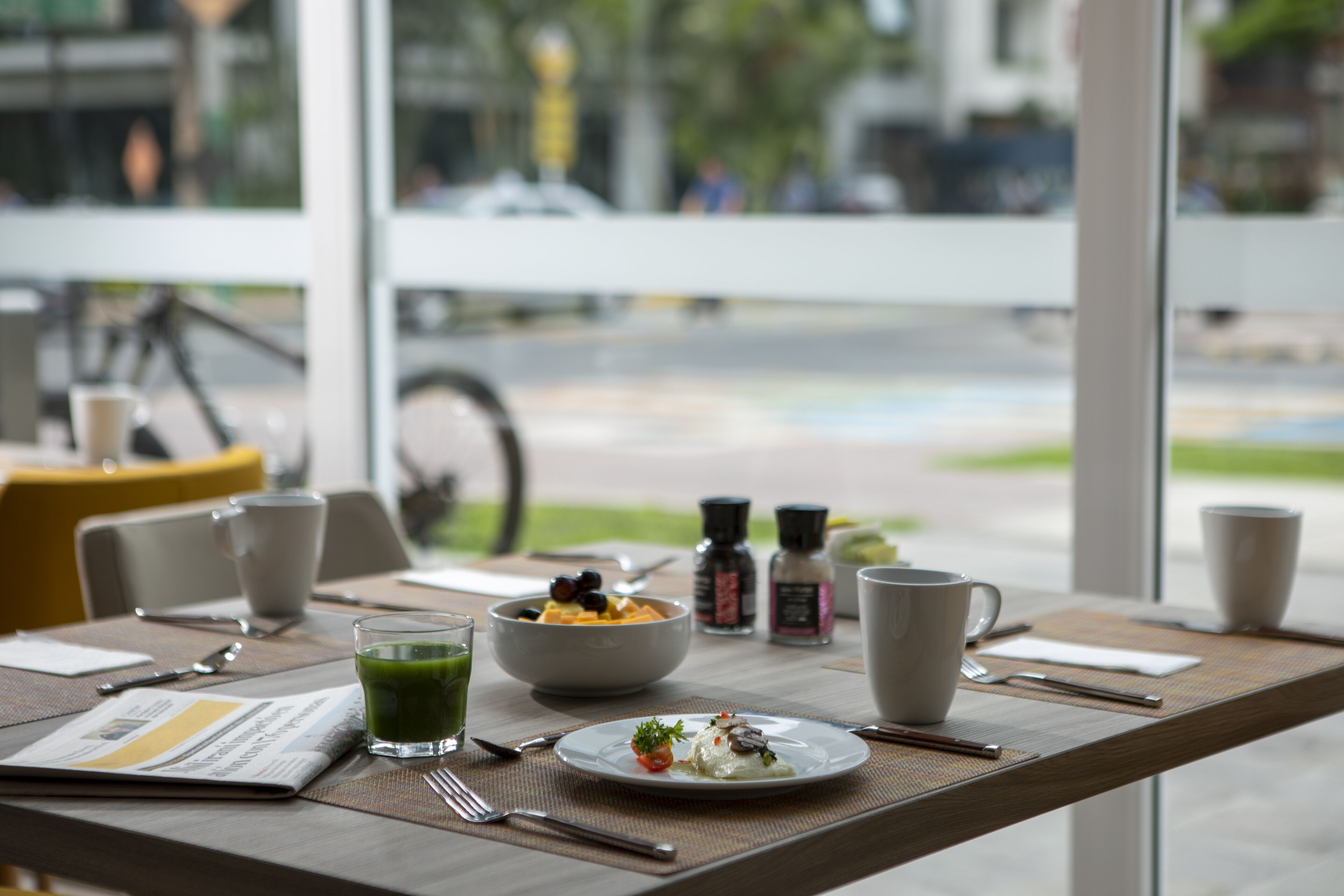 A dining table with a meal, cups, and a newspaper.