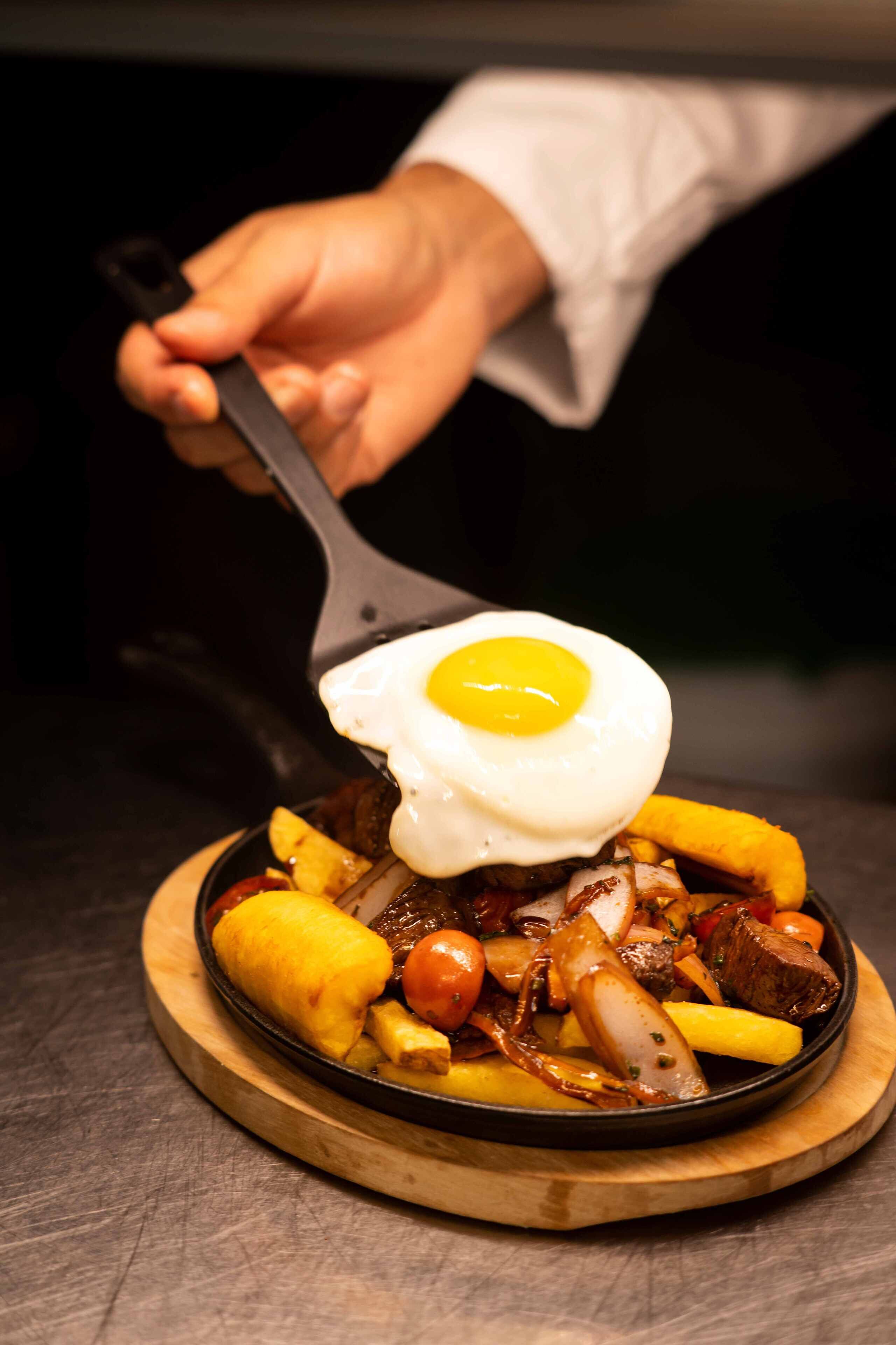Um cozinheiro servindo um prato com um ovo frito por cima.