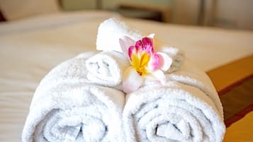 Une serviette blanche, soigneusement pliée, ornée d’une fleur décorative, est posée sur le lit.