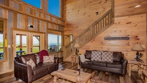 A spacious living room with two leather sofas, a wooden coffee table, and a staircase leading to an upper level.