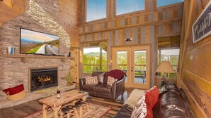 A cozy cabin interior with a stone fireplace, leather sofa, and a large TV mounted on the wall.