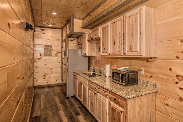 A compact kitchen with wooden cabinetry, a stainless steel refrigerator, a microwave, and a sink.