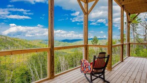 A wooden deck with a rocking chair and a view of a forested landscape.