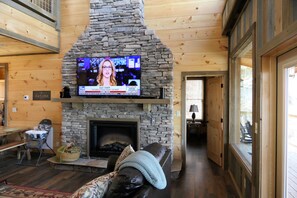 A cozy living room with a stone fireplace, a television mounted above it, and a comfortable seating area with a couch and a chair.