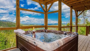 A hot tub on a wooden deck with a scenic view of a forest and mountains.