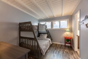 A bunk bed in a room with a wooden floor, a small table, a window with a view, and a wall-mounted air conditioner.
