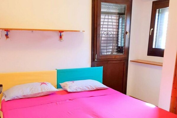 Un dormitorio con cama, ventana con persianas y puerta con reja de metal.