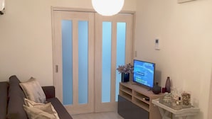 Uma sala de estar moderna com um sofá escuro, uma televisão de tela plana em um suporte e uma luminária de teto branca.