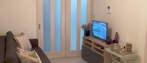 Uma sala de estar moderna com um sofá escuro, uma televisão de tela plana em um suporte e uma luminária de teto branca.
