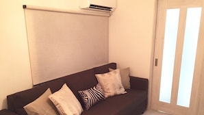 Um sofá marrom escuro com quatro almofadas em um quarto com piso de madeira clara e porta branca com painéis de vidro fosco.