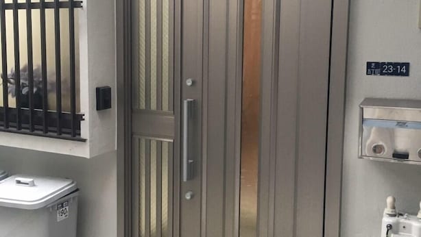 Entrada de um edifício moderno com porta de metal, uma pequena lixeira e uma caixa de utilidades à direita.