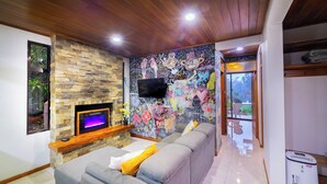 Una sala de estar con chimenea de piedra, un sofá gris, un televisor y un mural colorido en la pared.