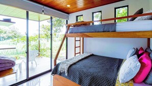 Un dormitorio moderno con una cama litera, una puerta corrediza de vidrio que da a un patio y un techo de madera.
