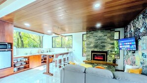 Una sala moderna con chimenea de piedra, un sofá gris y una zona de cocina con barra.