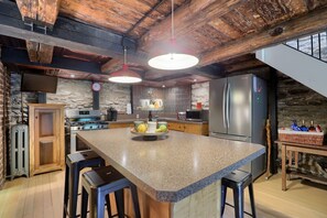 A kitchen with a granite island, bar stools, a stainless steel refrigerator, and a stone wall. - The Trolley House - A romantic getaway / 1 bedroom / 1 bath / 2 beds (Pequea)
