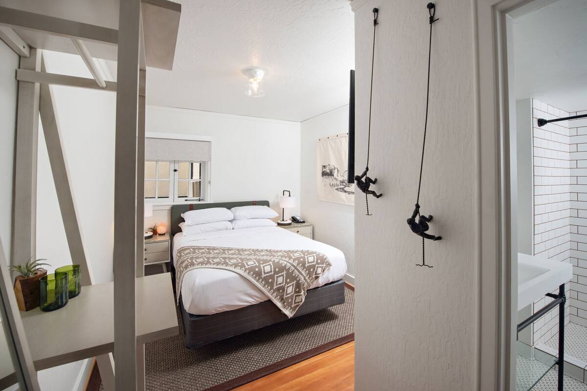 A modern hotel room with a bed, bedside table, lamp, and a wall-mounted hanging chair.