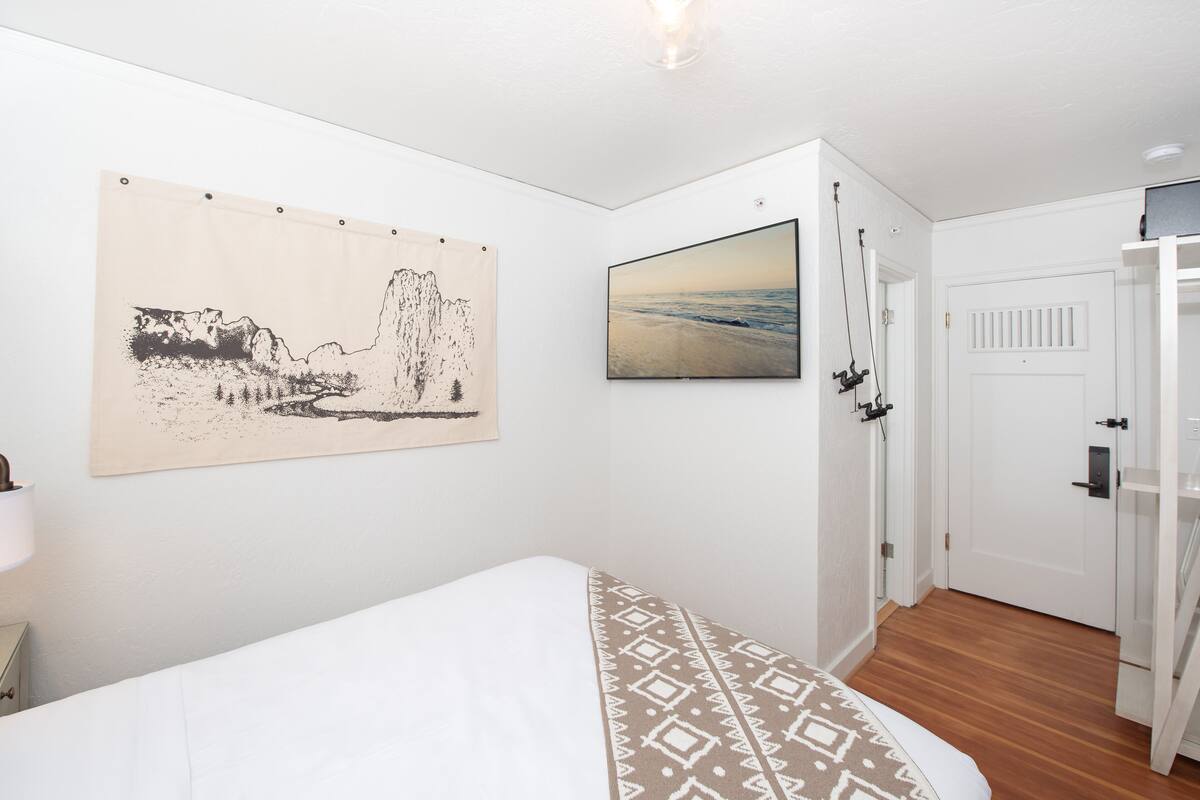A bedroom with a bed, a wall-mounted artwork, a television, and a door.