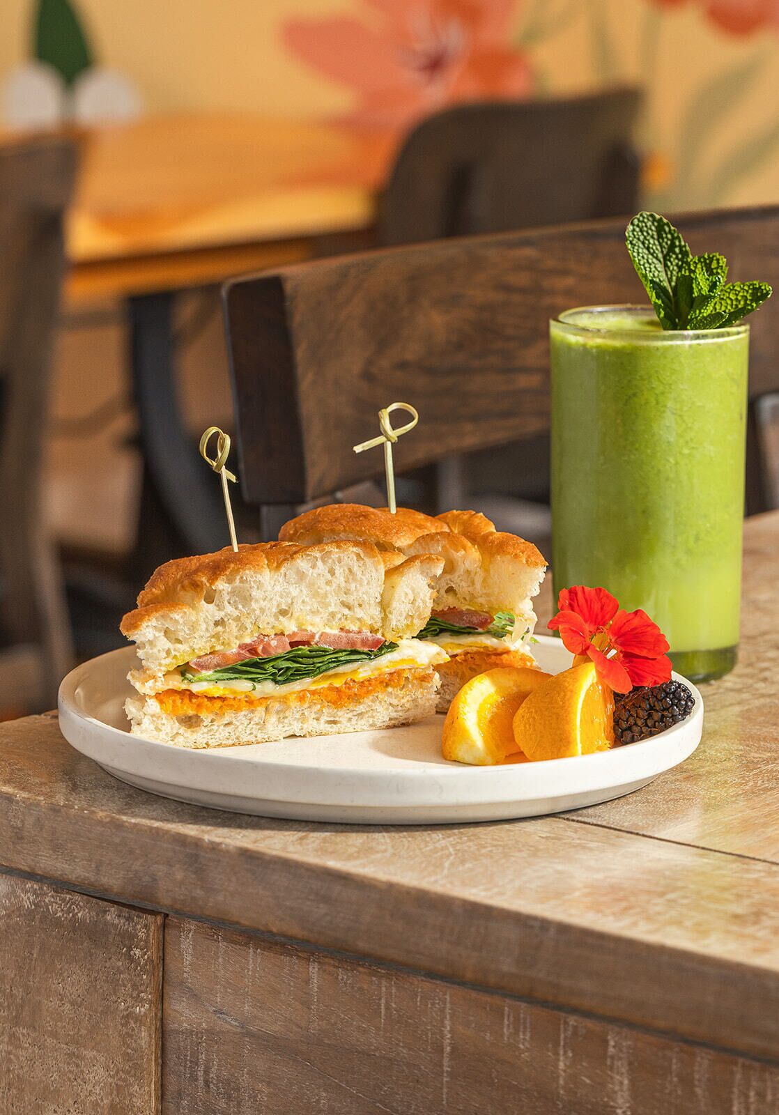 Een bord met een sandwich, een groen drankje en fruit op een tafel.