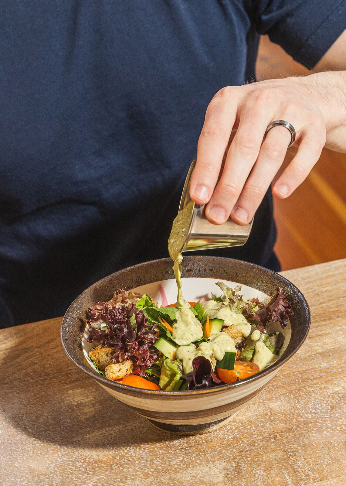 A person pouring dressing over a salad in a bowl.