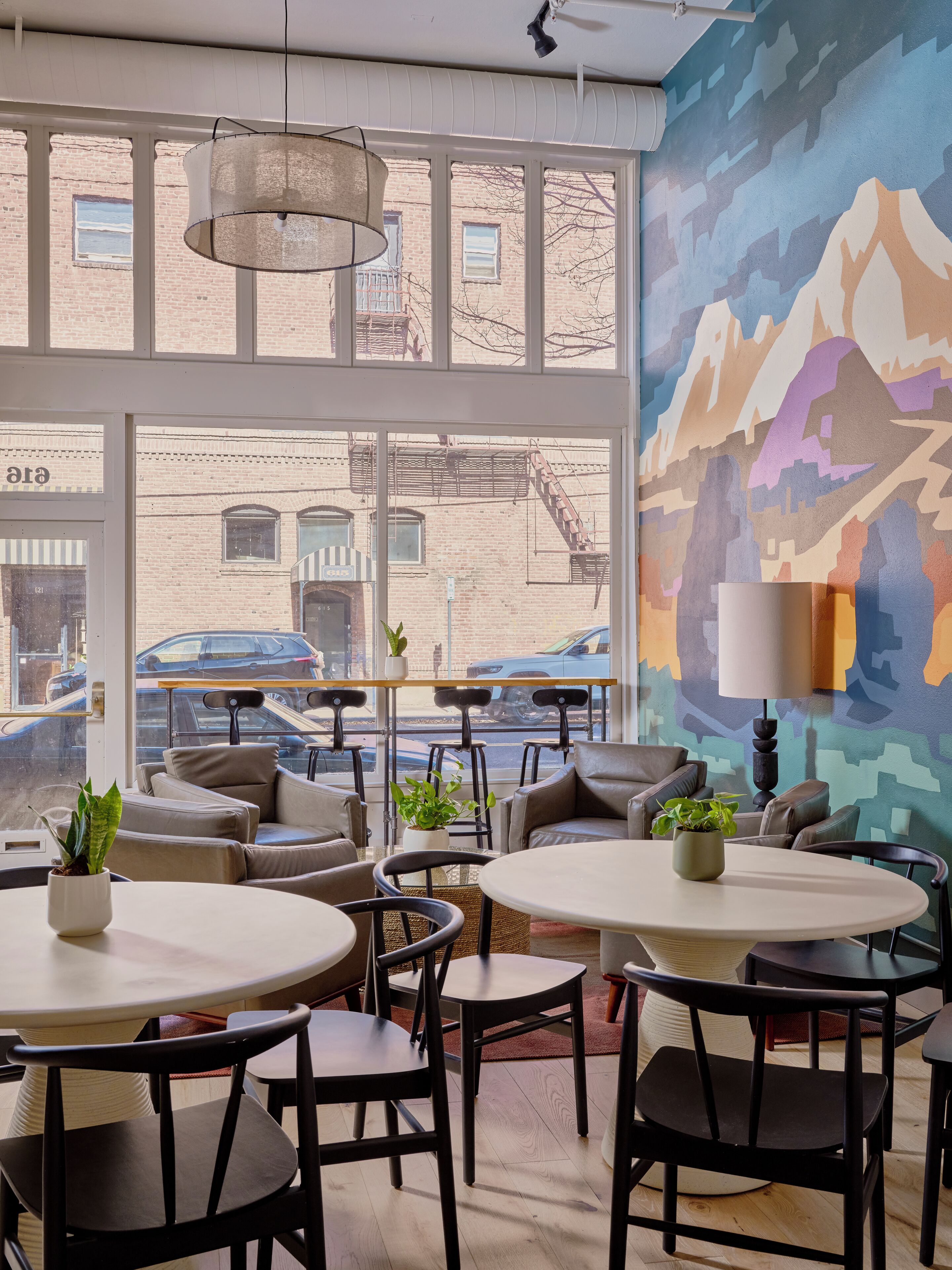 A cafe with round tables, black chairs, and a large window overlooking a street.