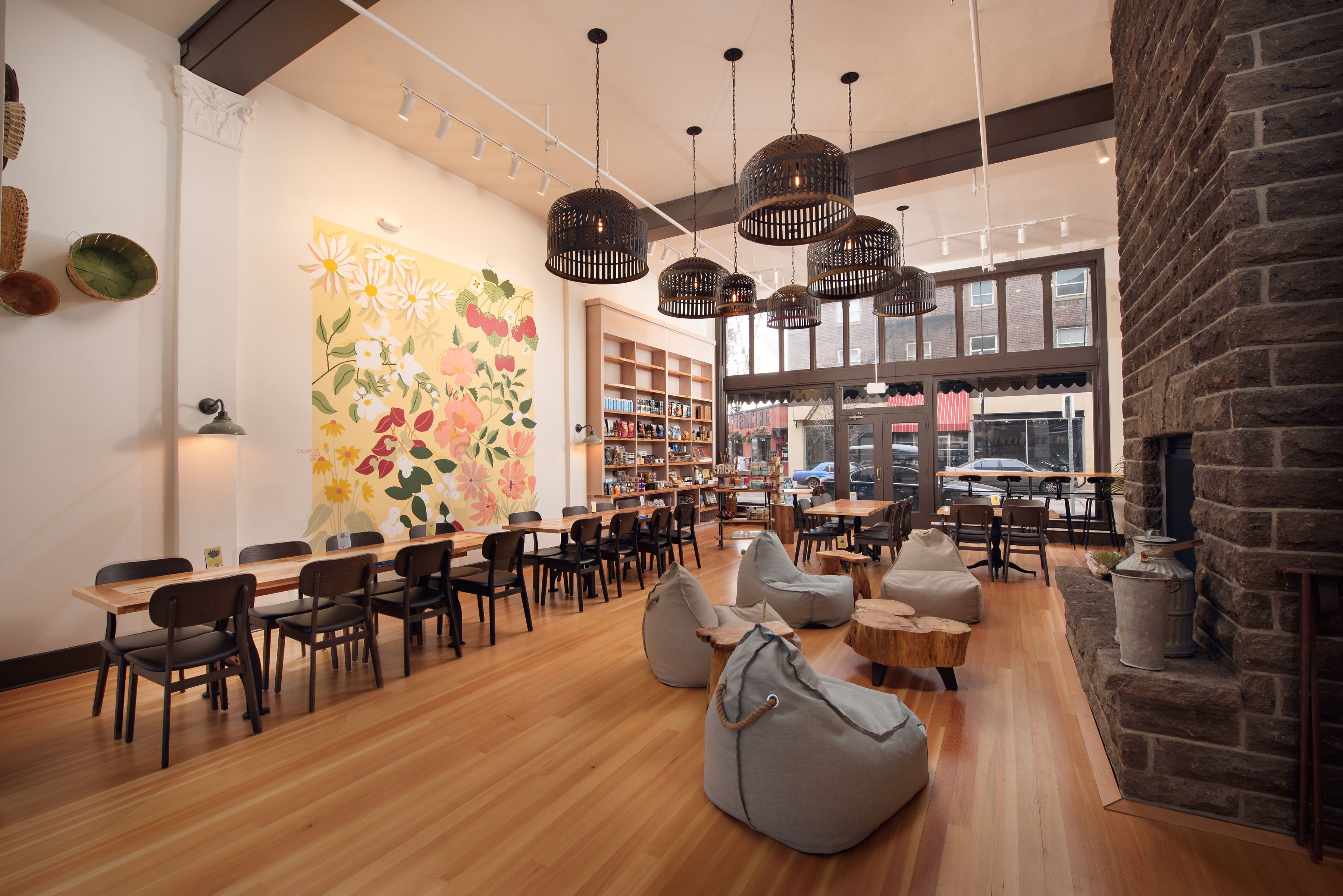 A spacious cafe with wooden tables and chairs, a large floral mural, and a brick wall.